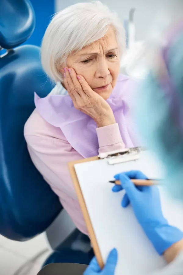 an elderly woman cupping her jaw due to tooth pain
